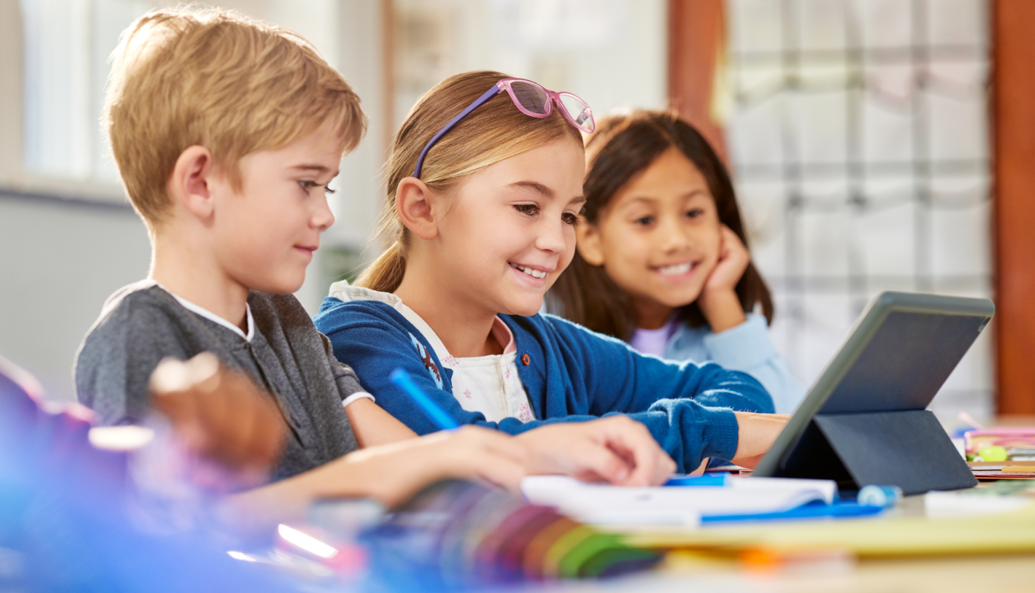 bērni šēz pie galda skatās planšetē 