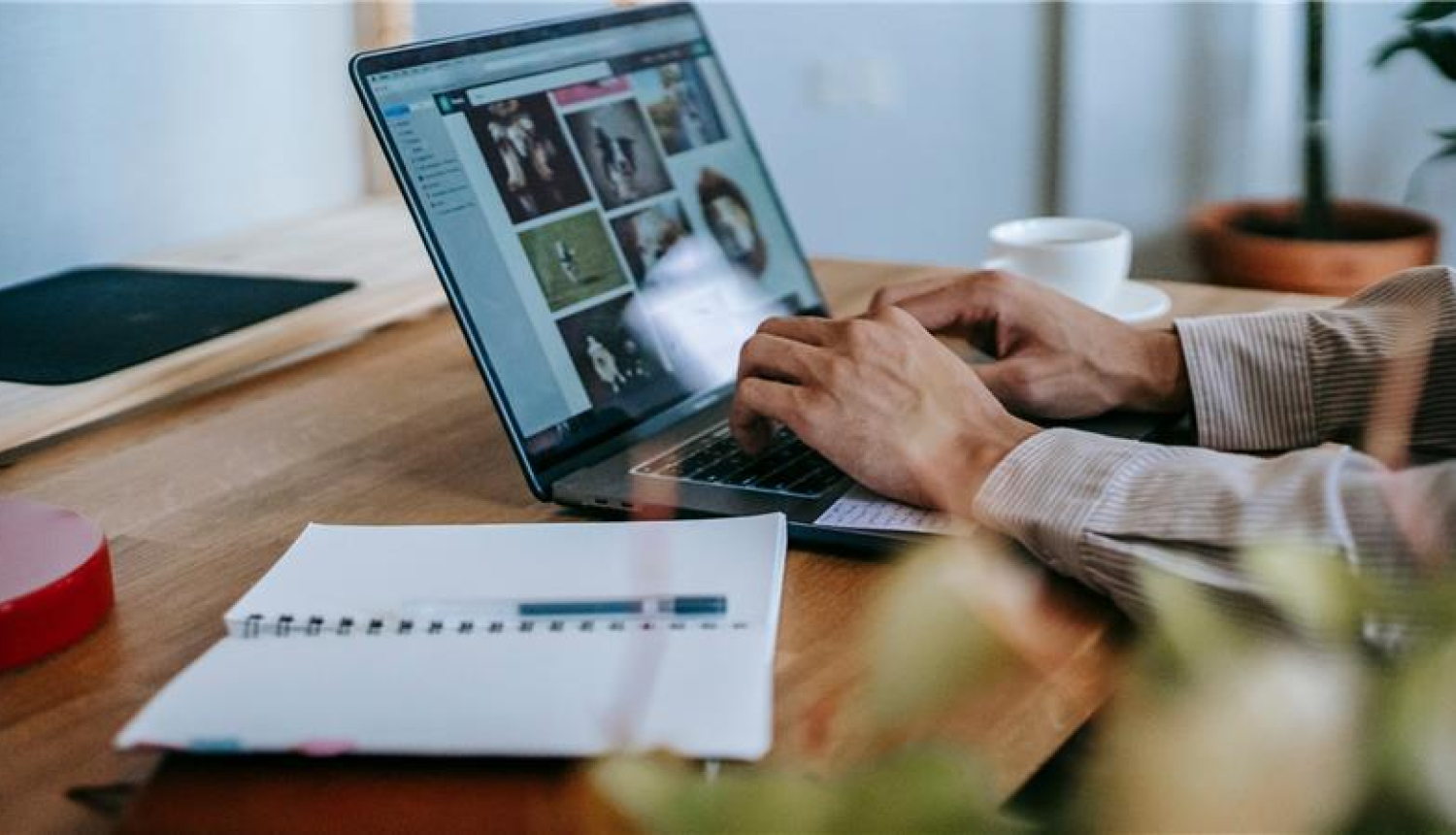 cilvēks strādā pie galda ar portatīvo datoru, blakus uz galda ir pierakstu klade