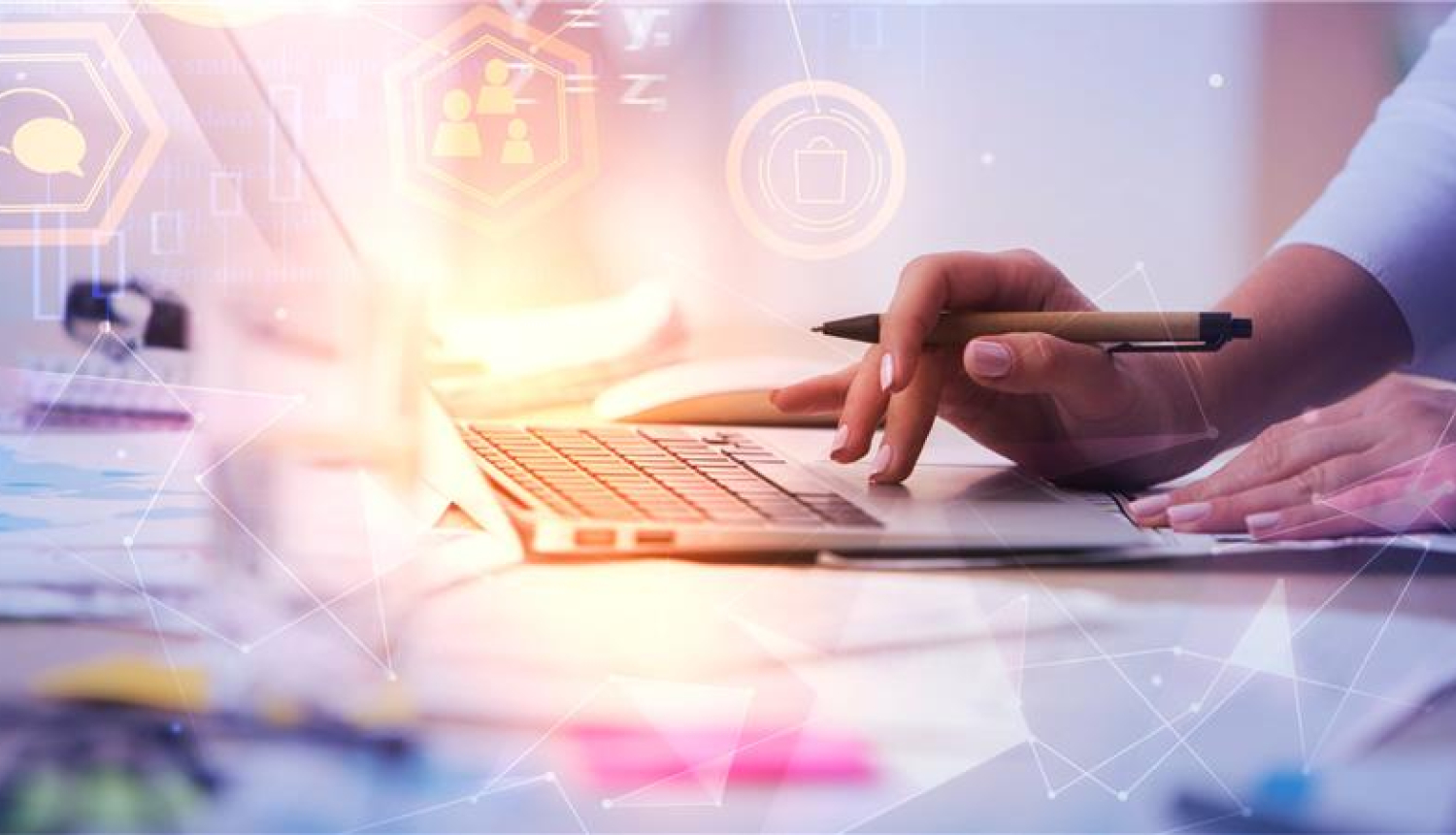 uz galda atvērts portatīvais dators, sievietes rokas raksta uz tastatūras un tur rokā pildspalvu, priekšā ir uzlikti bildei grafiski elementi