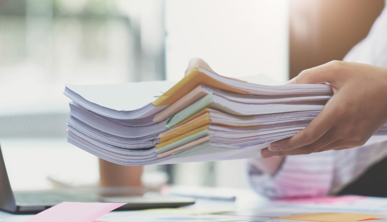 sieviete tur rokās kaudzi ar drukātiem dokumentiem virs galda