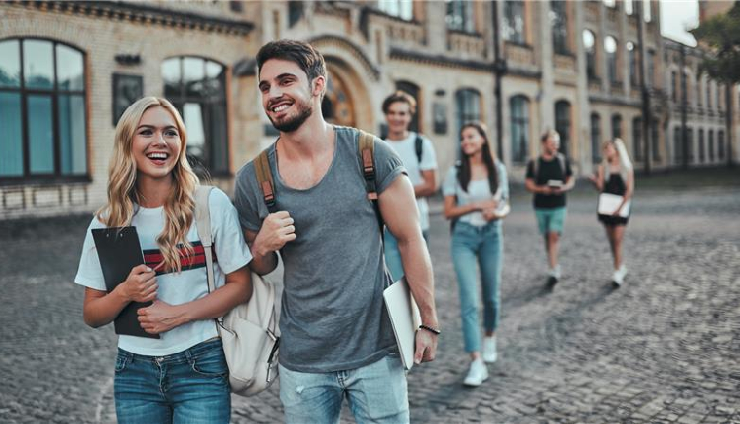 divi studenti iet pa ceļu blakus universitātei, rokās mapes