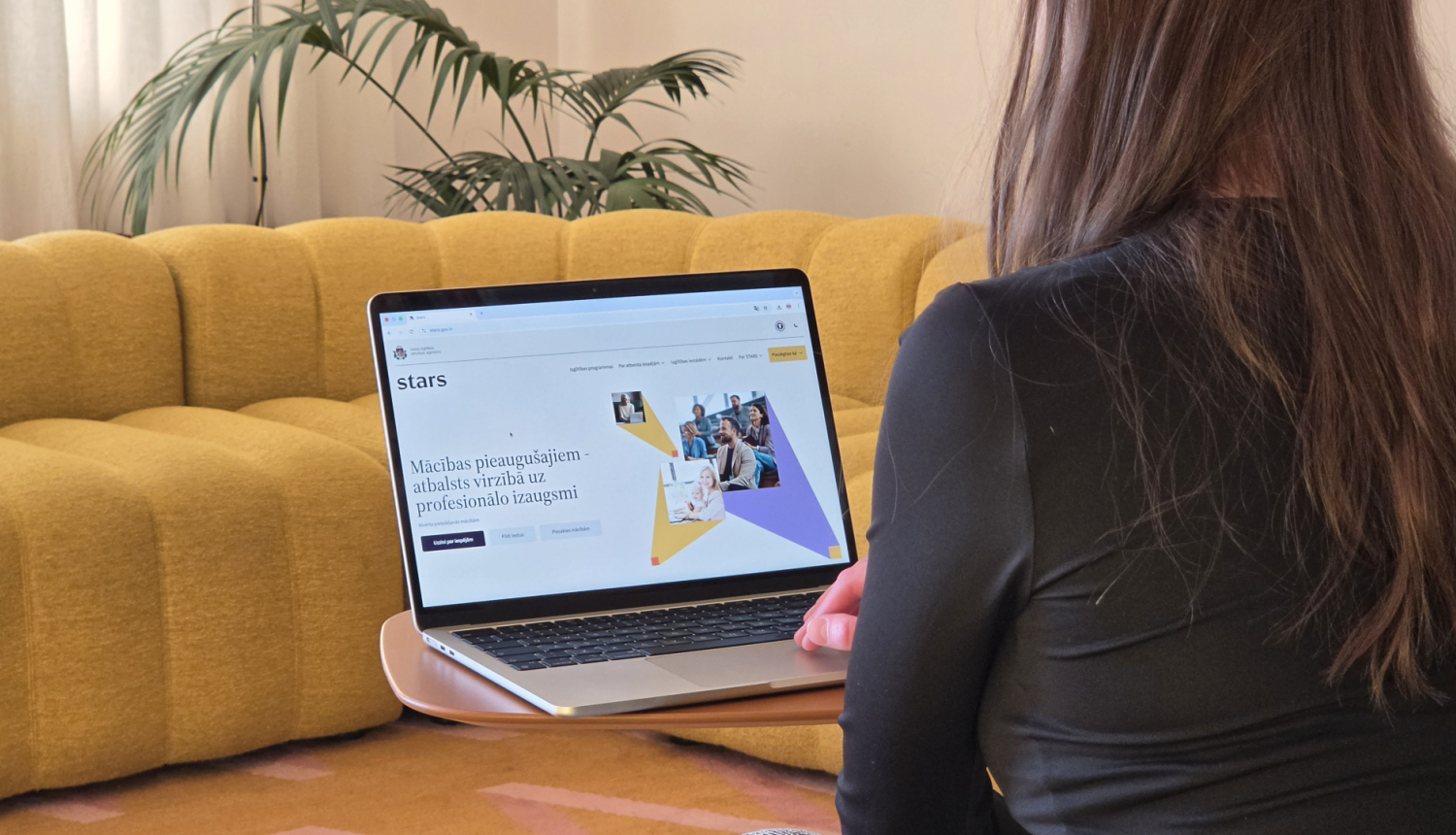 Esi Starā, sieviete sēž ar muguru, klēpi viņai atvērts dators, kur uz ekrāna ir redzama www.stars.gov.lv mājaslapa