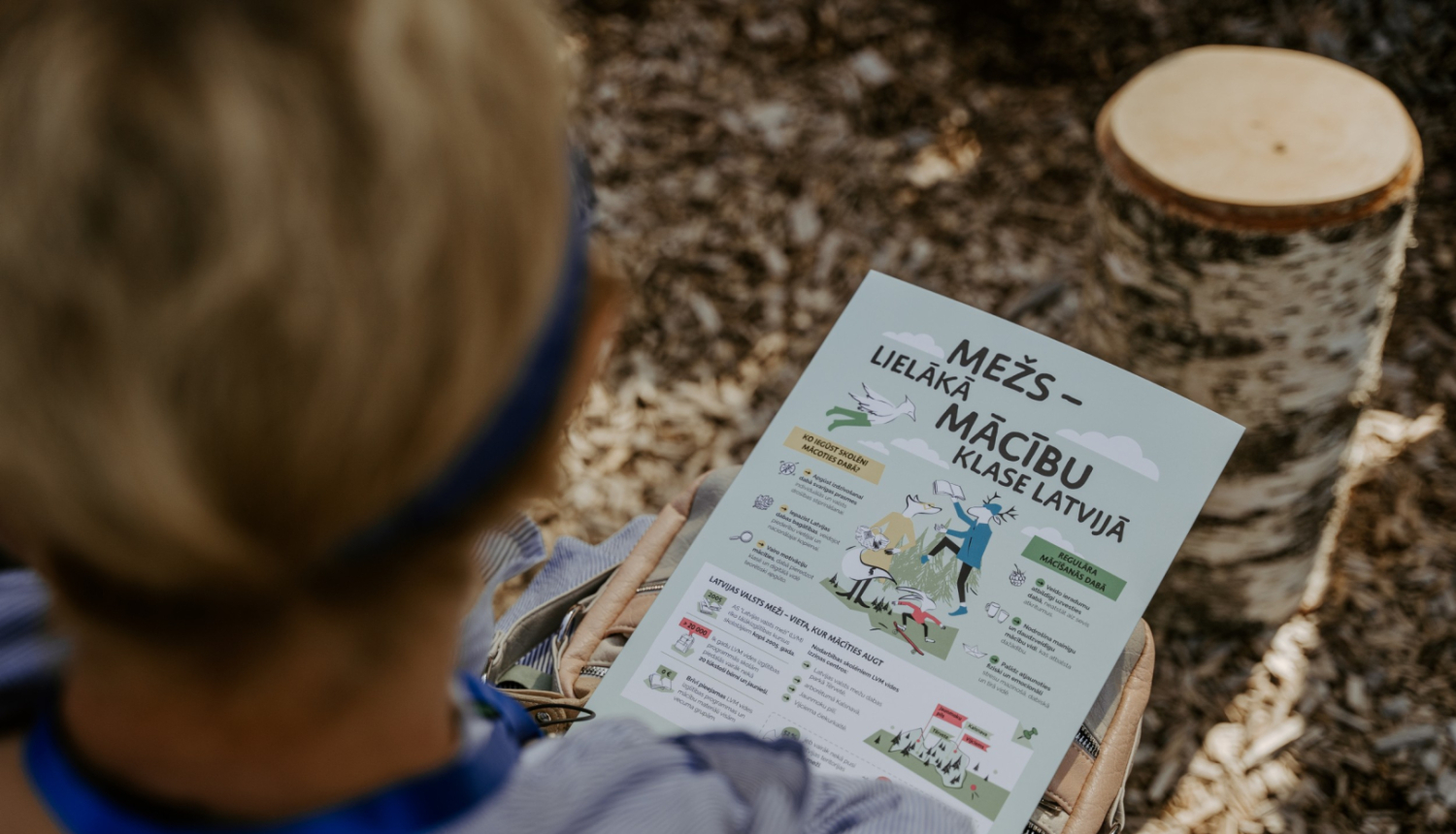 berns sez mežā ar plakātu rokās, uz kura rakstīts "Mežs - lielākā māčibu klase"