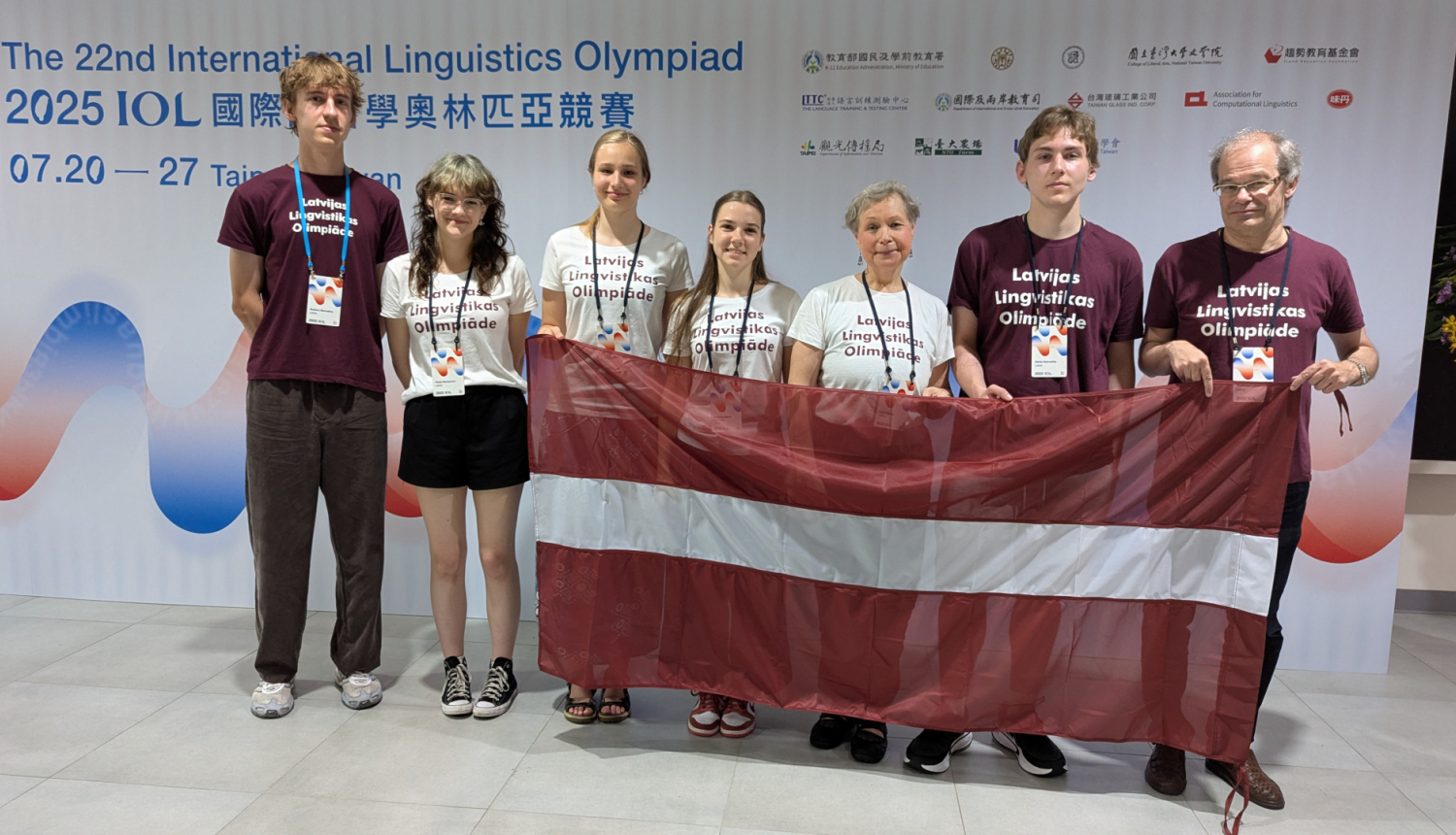 Starptautiskās Lingvistikas olimpiādes dalībnieki no Latvijas visi kopā stāv un tur karogu