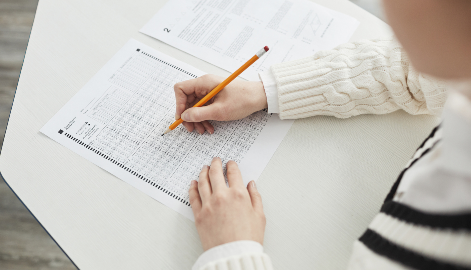 skolniece pilda testu ar zīmuli pie galda