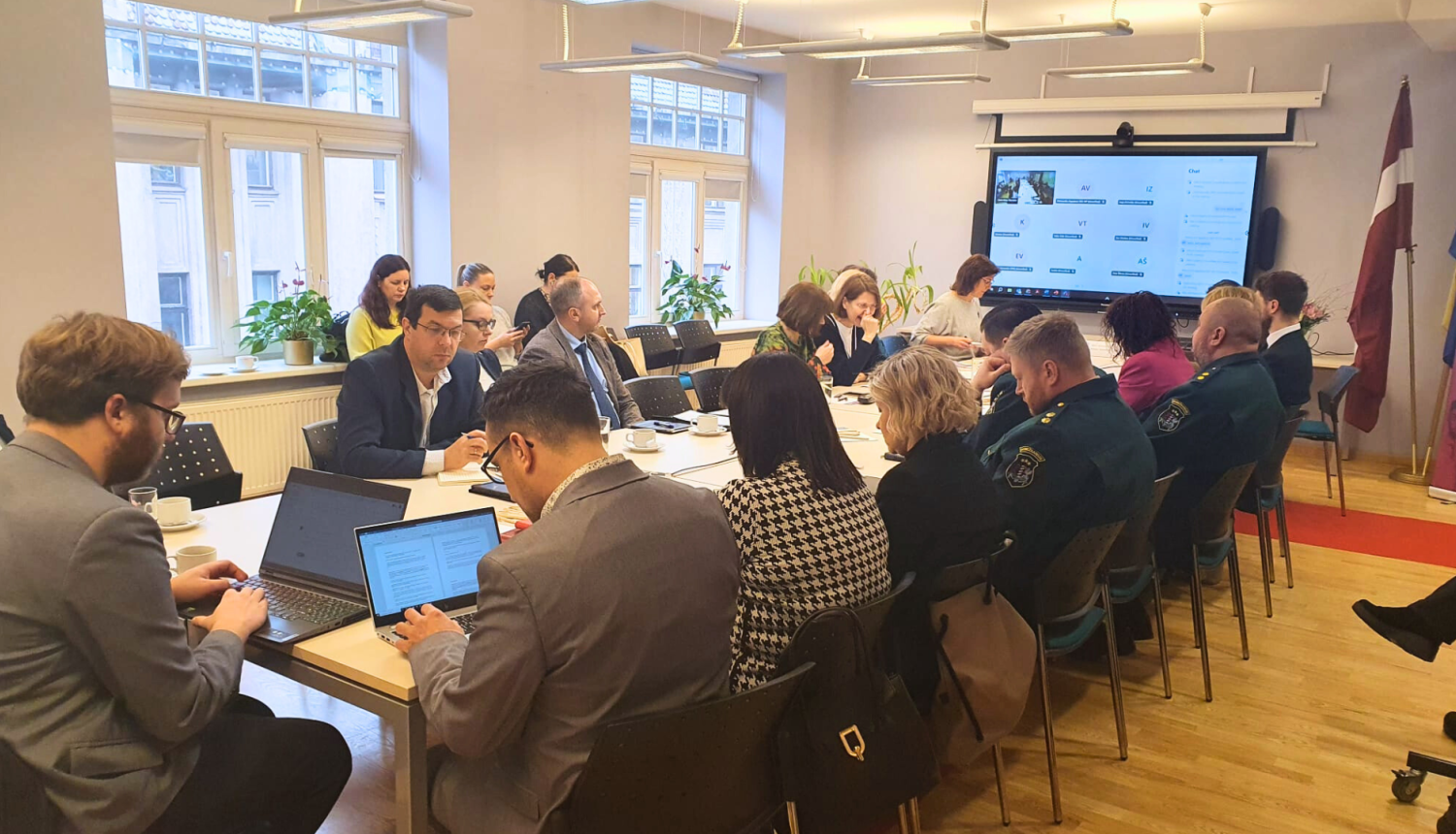 Cilvēki zālē sēž pie galdiem