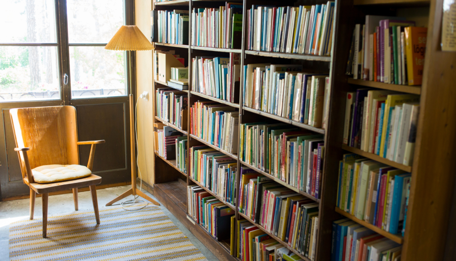 bibliotēkas gramatu plaukti blakus kresls ar stāvlampu lasīšanai