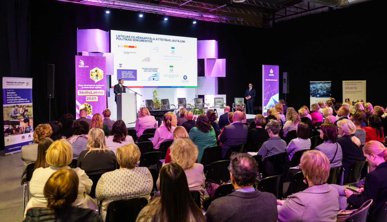 Cilvēki zālē klausās konference