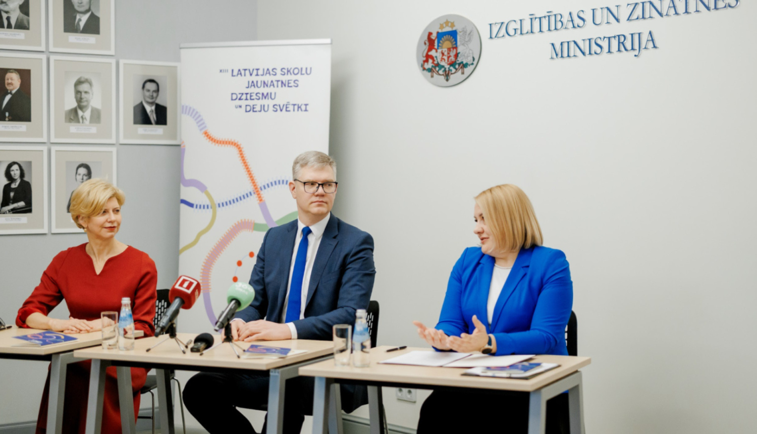 Cilvēki preses konferencē sēž pie galda un runājas