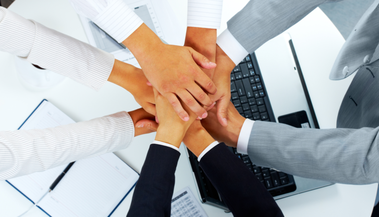 Cilvēki biznesa vidē salikuši rokas vienu otrai virsū