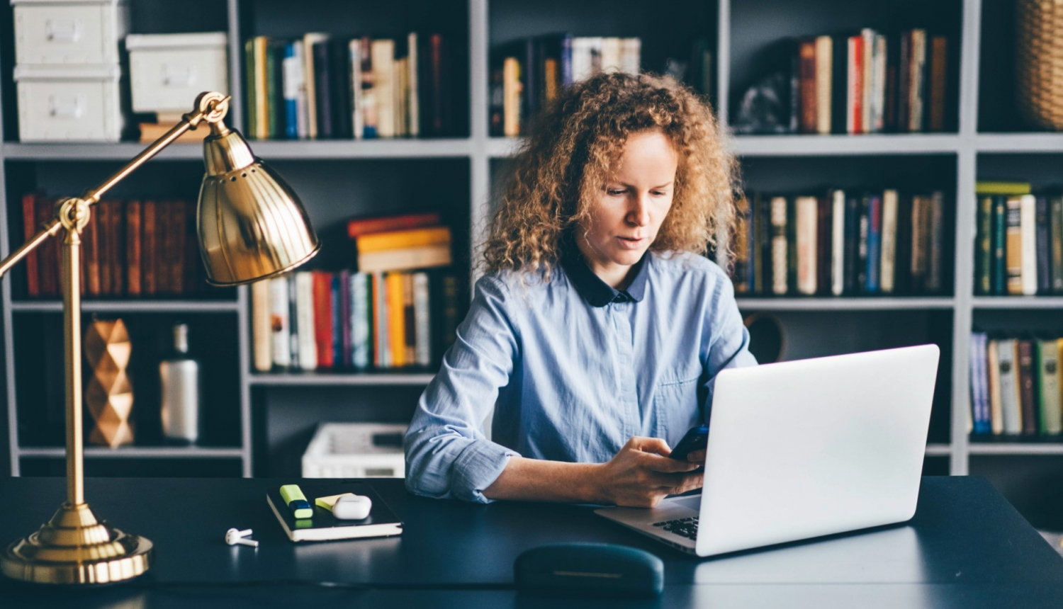 sieviete strādā pie portatīvā datora pie galda bibliotēkā