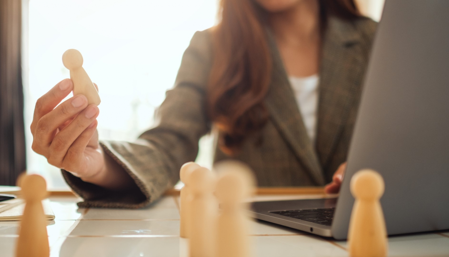 sieviete strādā pie darba galda, uz galda portatīvais dators un balkus šaha figūras, sieviet rokā tur šaha figūru