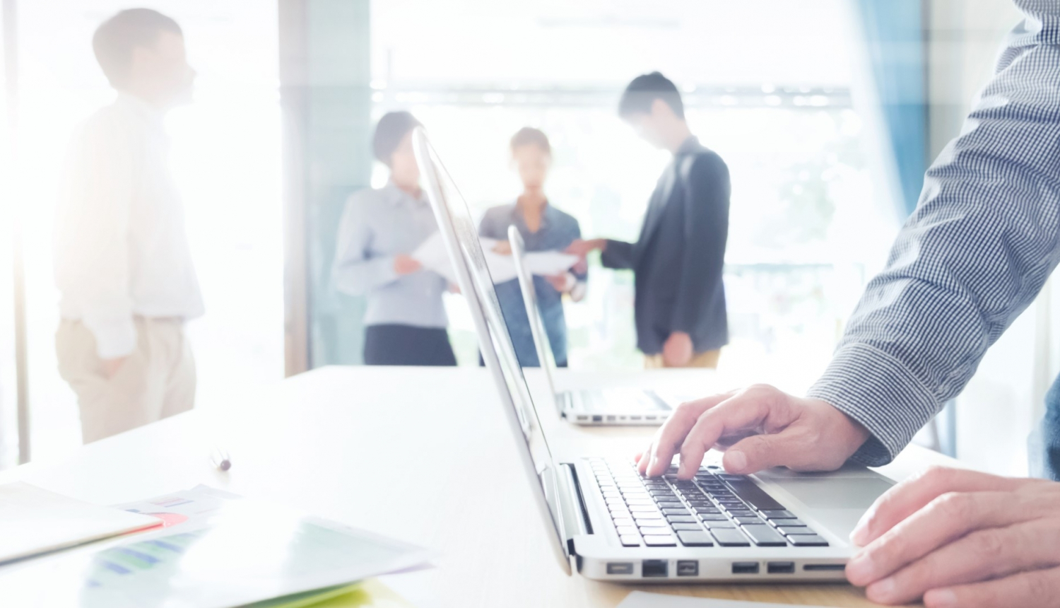 biroja telpā virietis stradā pie portatīvā datora aizmugurē stāv kolēģi