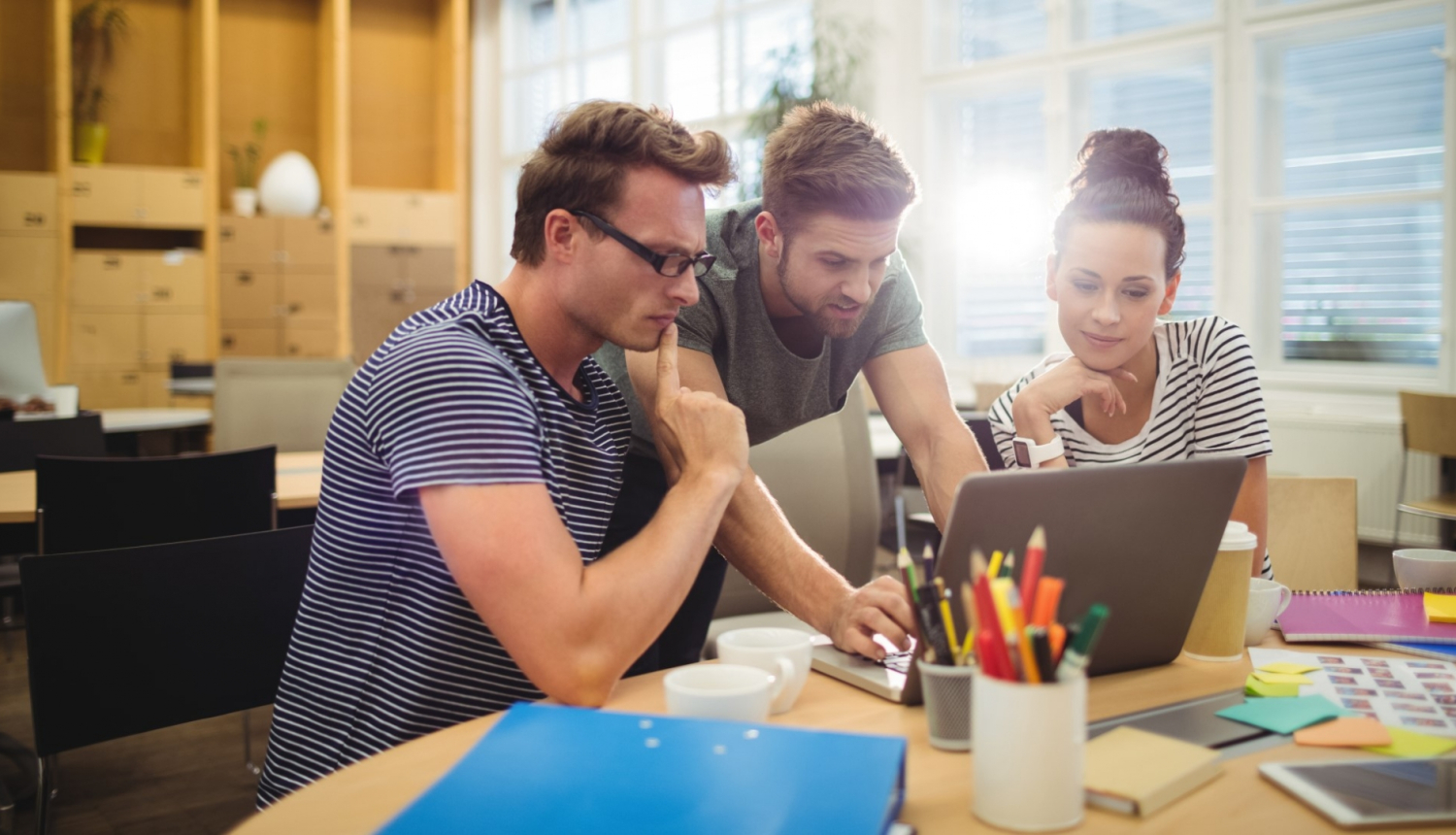 divi vīrieši un viena sieviete strādā kopā pie viena datora