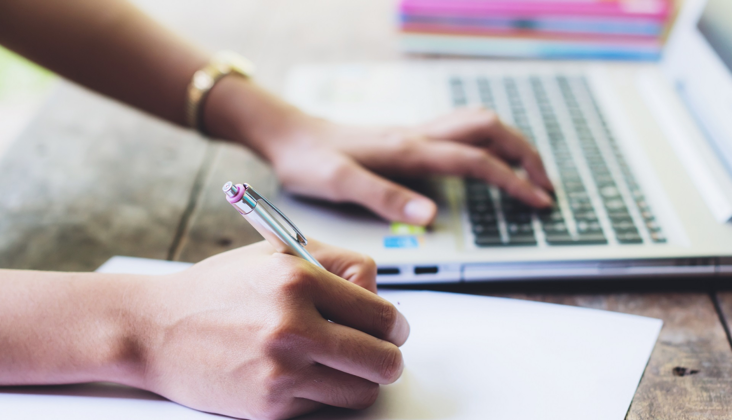 Cilvēka roka tuvplānā veic pierakstus un spiež datora tastatūras pogas