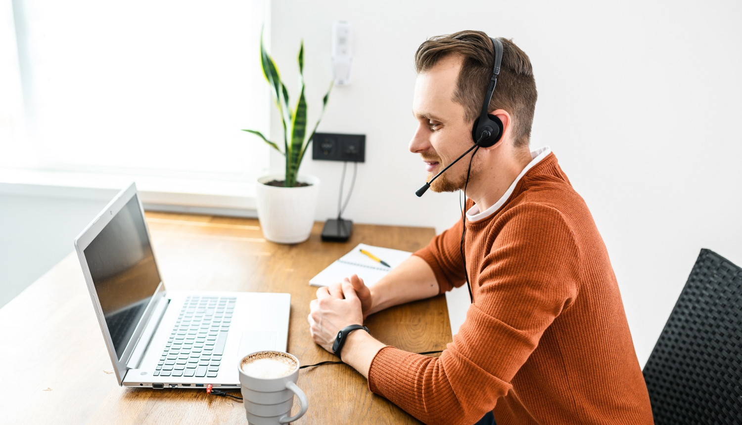 Vīrietis klausās tiešsaistes semināru, sēžot pie galda