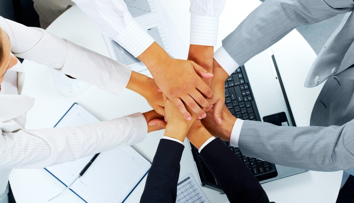 Četri cilvēki sadevušies rokās, fonā redzami dokumenti un klēpjdators