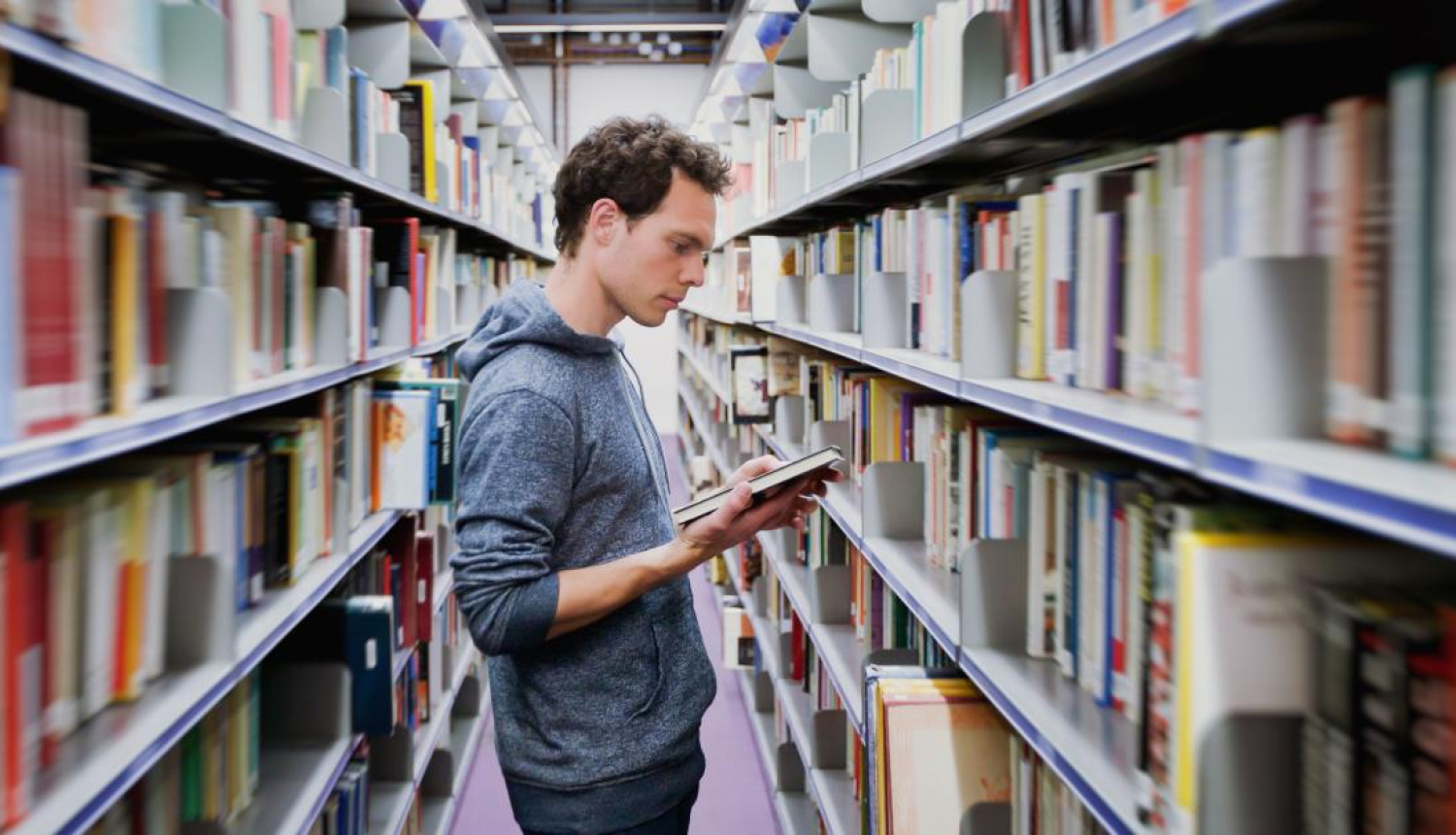 Cilvēks bibliotēkā lasa grāmatu