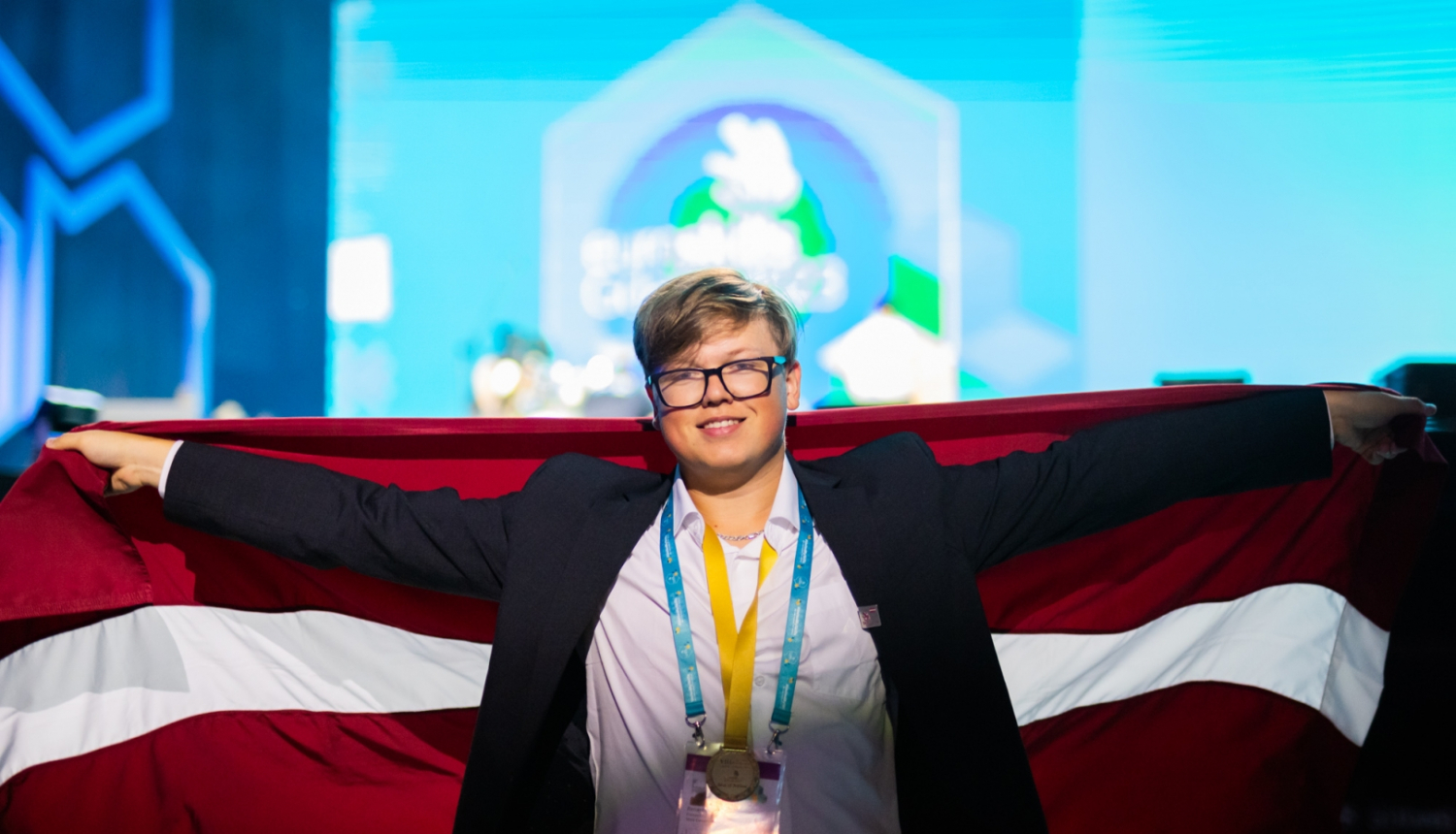 Jauns puika ar Latvijas karogu aiz muguras un ar medaļu