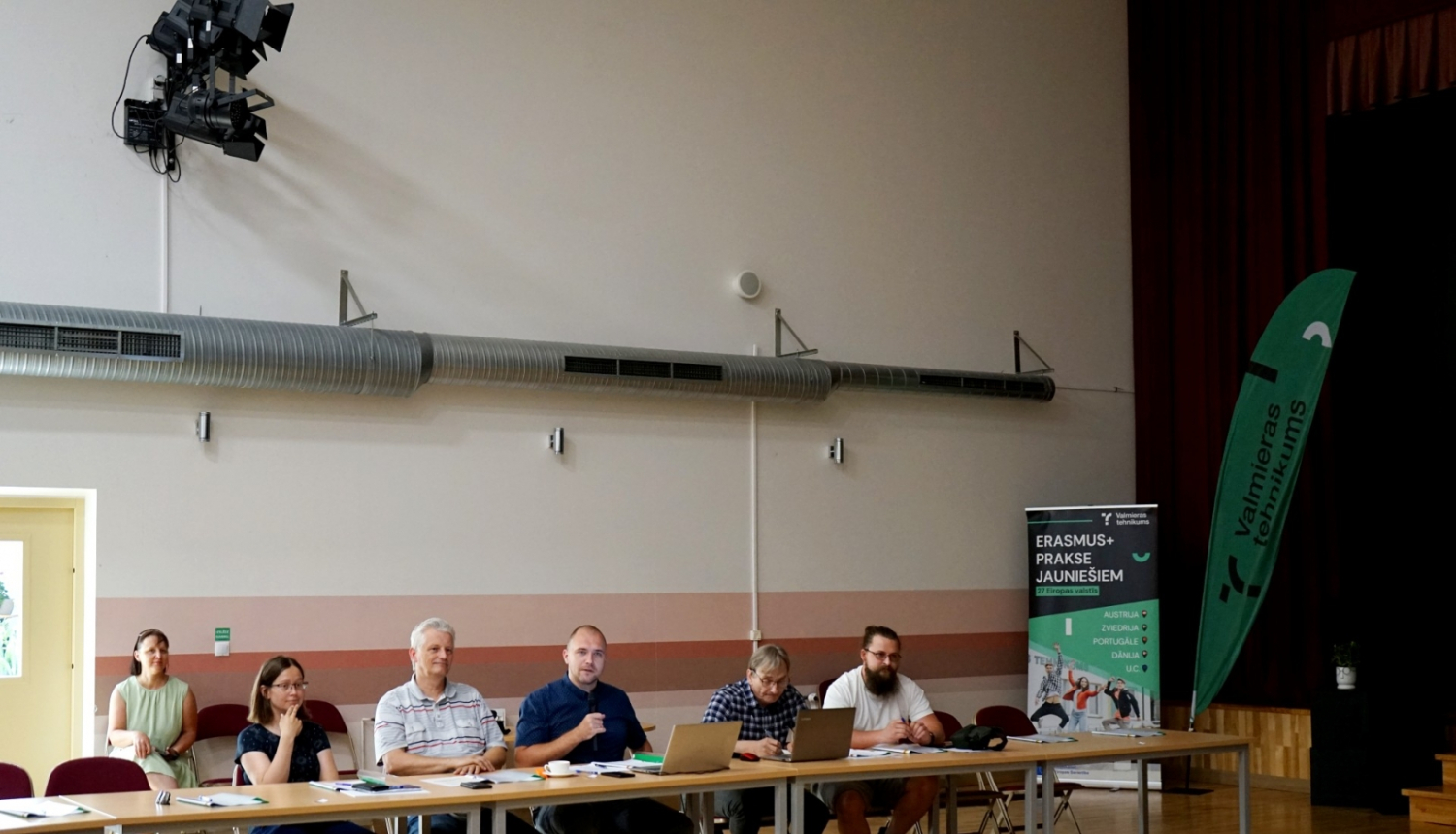 Cilvēku grupa sēž pie galva lielajā sporta hallē