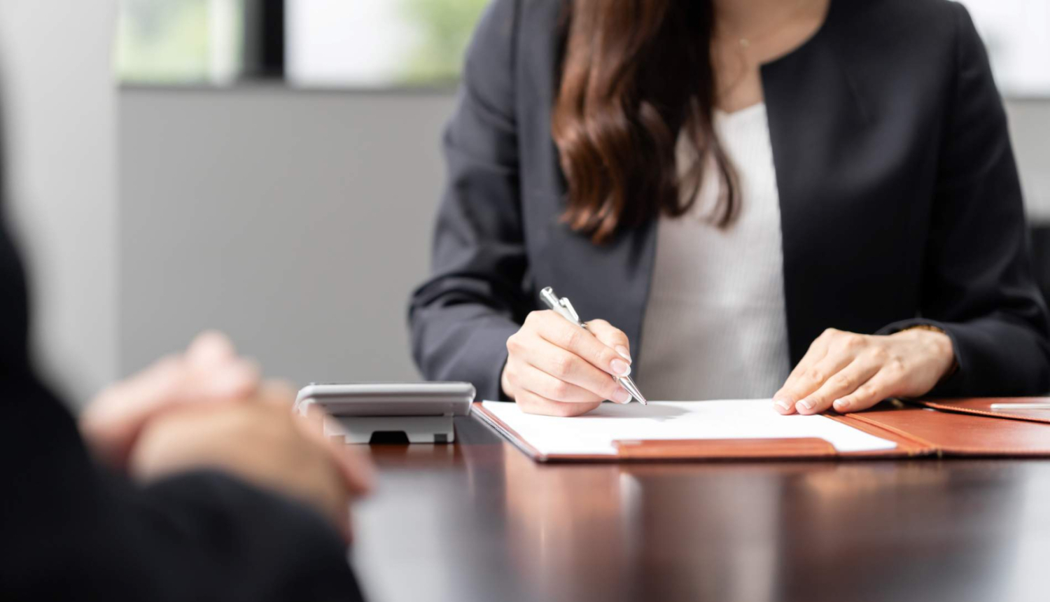 sieviete pieraksta uz papīra lapas piezīmes darba intervijā, pretī viņai sēž intervējamais