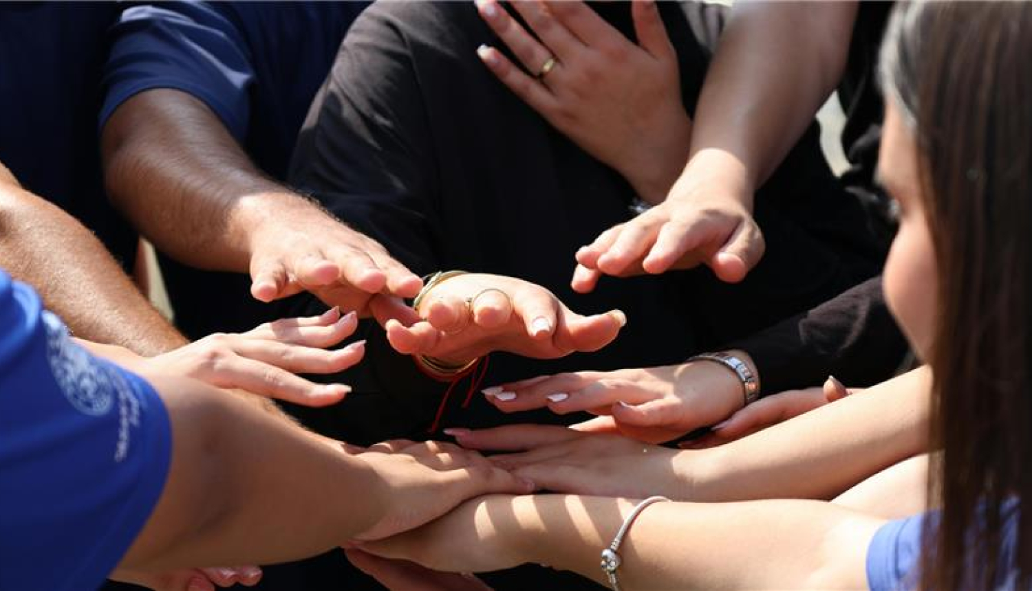 Erasmus vairāki cilvēki stāv aplī un saliek rokas kopā centrā