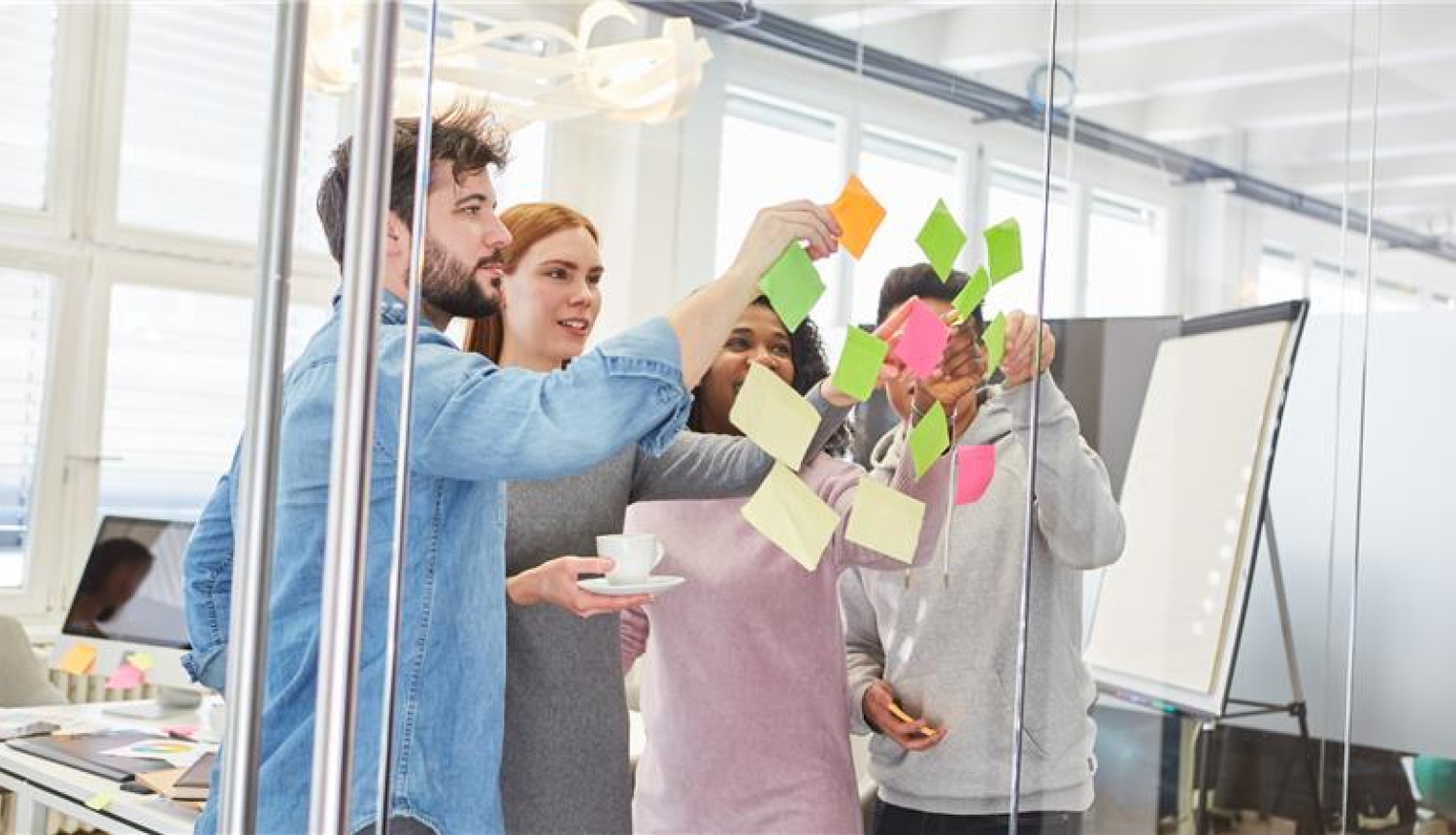 cilvēku grupa stāv pie stikla sienas un līmē krāsainas piezīmju lapiņas