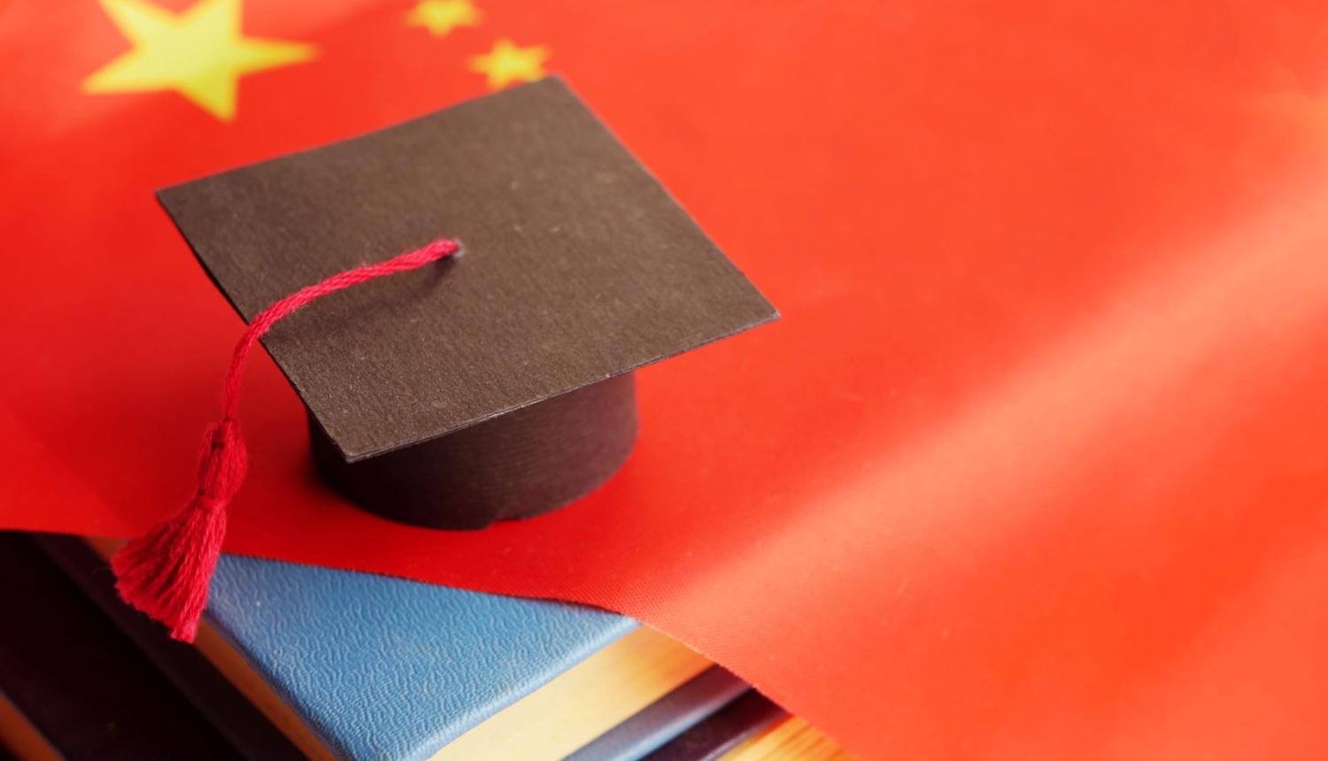 Kinas karogs nolikts uz galda viršu grāmatām, tasm virsū maza augstskolas absolventa cepure